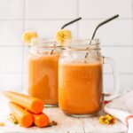 Two mason jar mugs filled with carrot cake smoothie with stainless steel straws.