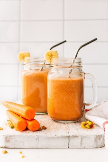 Two mason jar mugs filled with carrot cake smoothie with stainless steel straws.