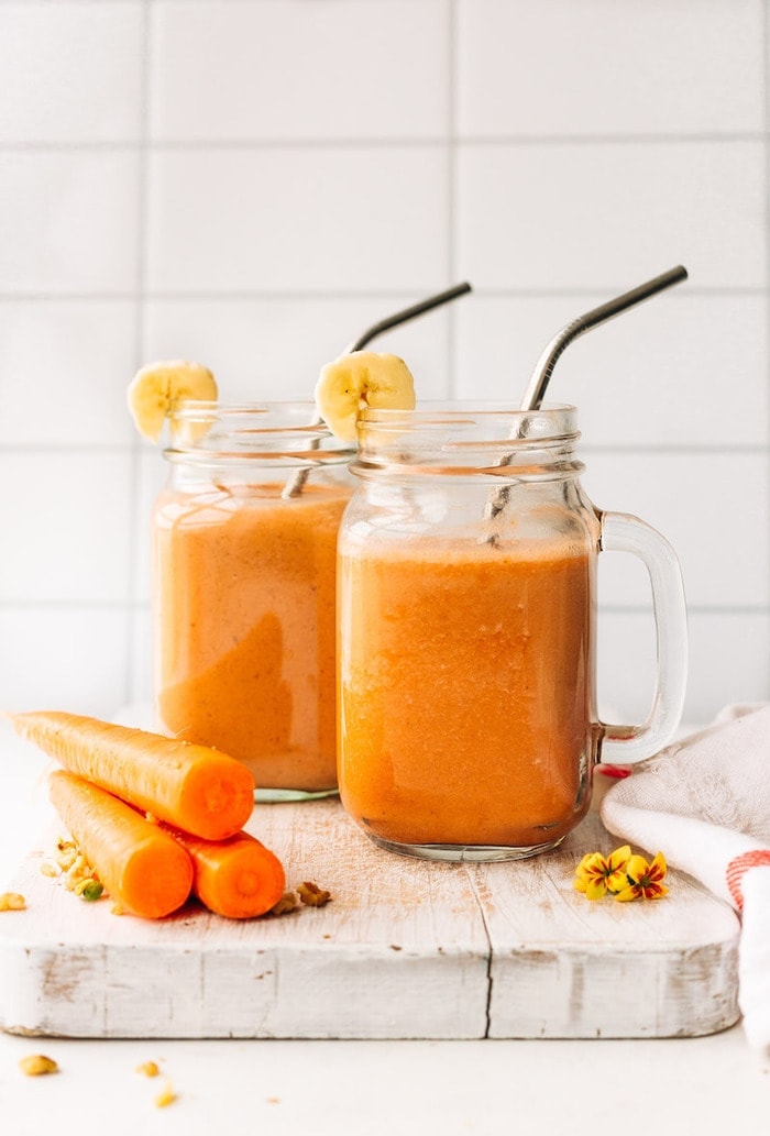 Two mason jar mugs filled with carrot cake smoothie with stainless steel straws. 