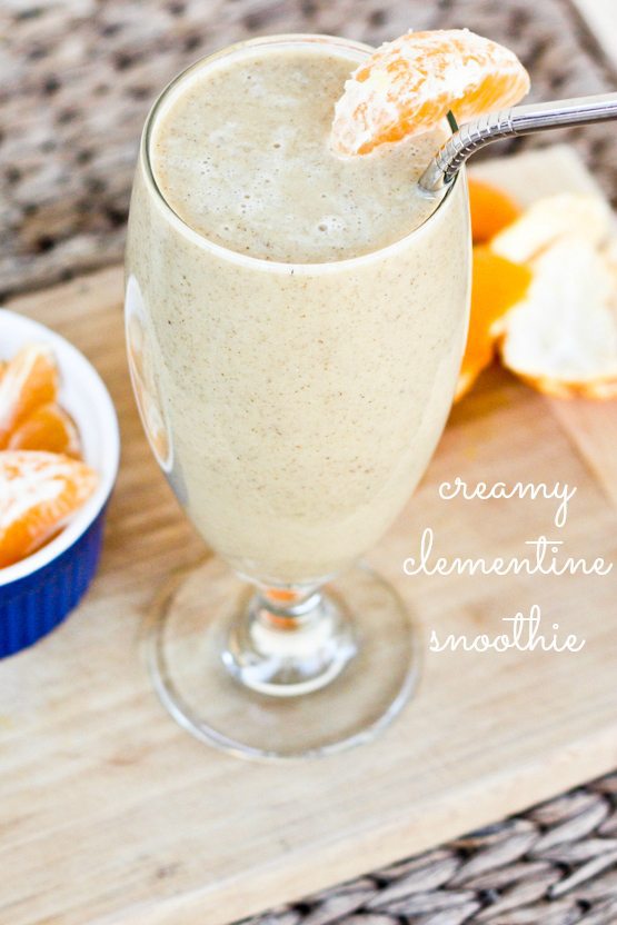 Creamy Clementine Smoothie served in a tall clear glass on wood cutting board with clementine slices.