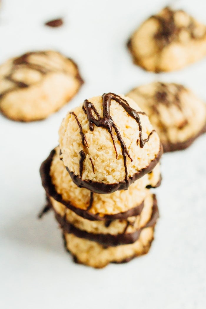 A stack of macaroons drizzled with dark chocolate. A few macaroons are out of focus in the background.