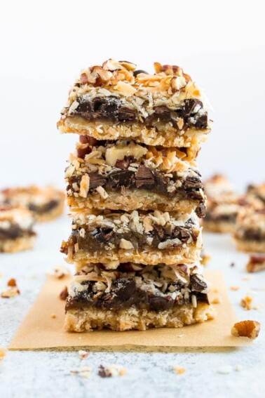 A stack of healthier magic cookie bars. An almond flour coconut crust, topped with coconut caramel, coconut flakes, pecans and chocolate chips.
