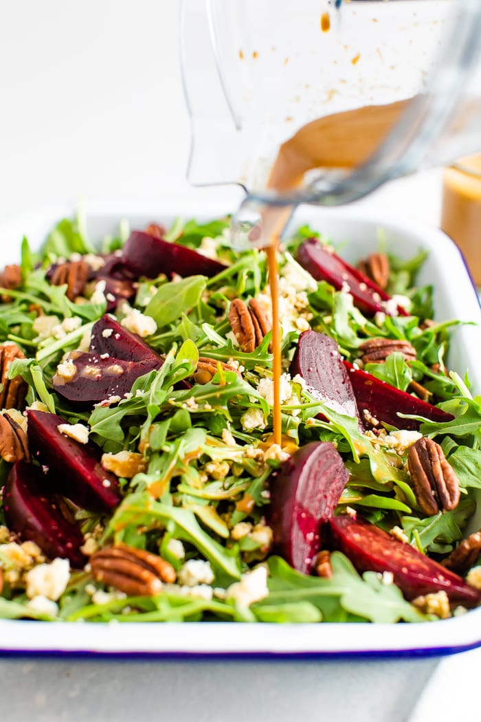 Balsamic dressing being poured over an arugula salad with beets, pecans and gorgonzola.