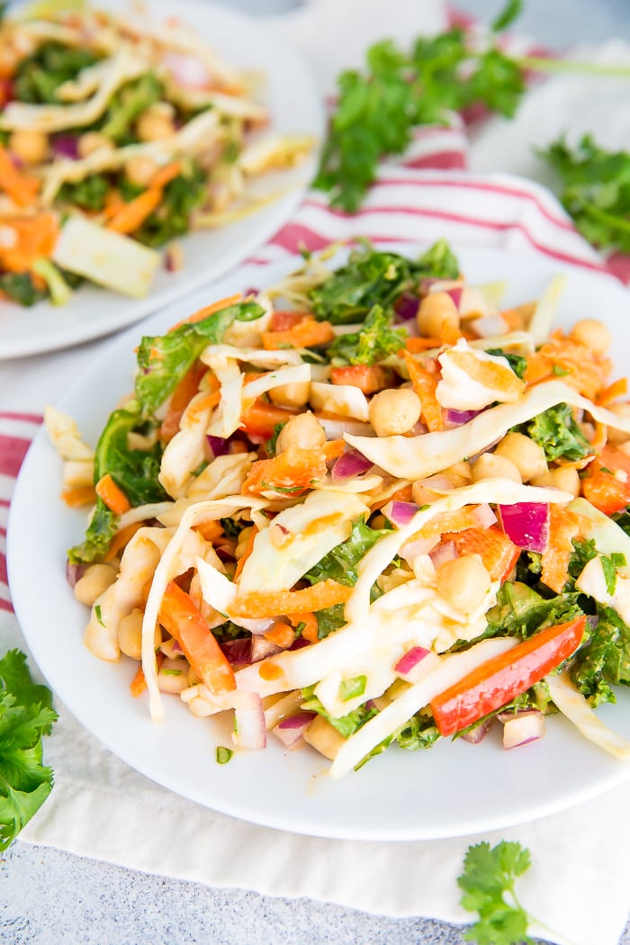 Kale and cabbage pad thai salad on a plate with peppers, onions and chickpeas. Another plate is in the background.