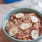 Banana Almond Teff Porridge in a light blue bowl. Almondmilk container in background.