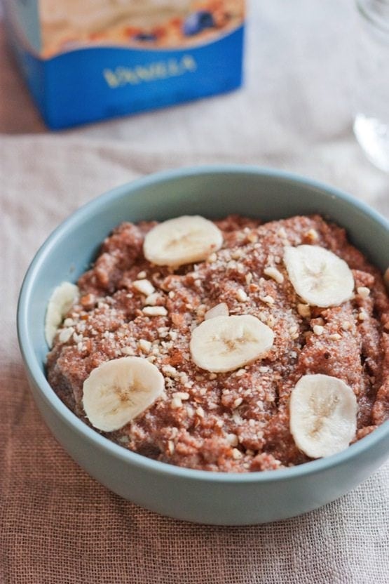 Banana Almond Teff Porridge in a light blue bowl. Almondmilk container in background.