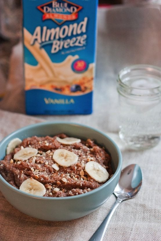 Banana Almond Teff Porridge in a light blue bowl. Almondmilk container in background.