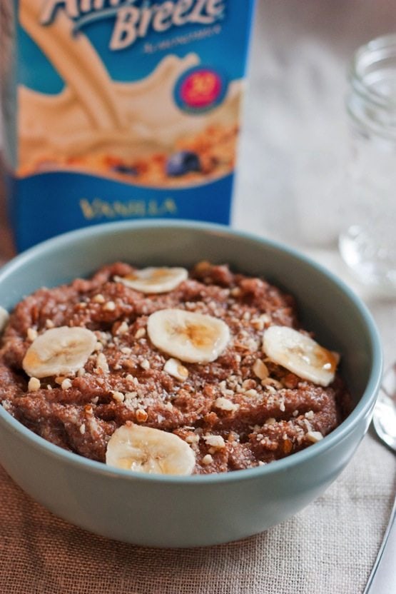 Banana Almond Teff Porridge in a light blue bowl. Almondmilk container in background.