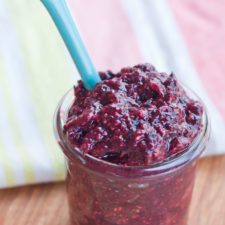 Mixed Berry Chia Seed Jam served in a small clear glass jar with light blue serving spoon.