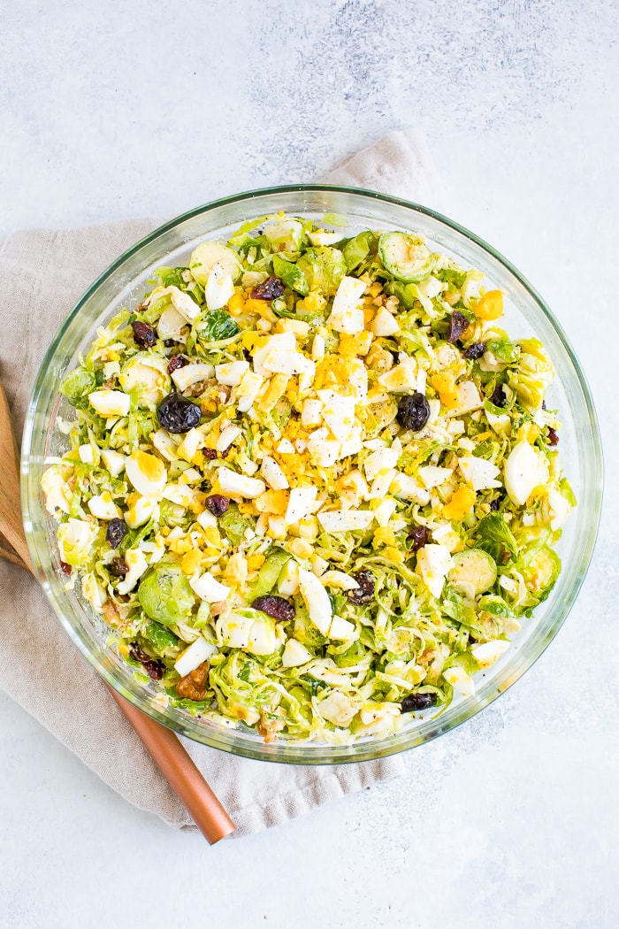 A healthy Brussel sprout chopped salad with cranberries, egg, feta, and walnuts.