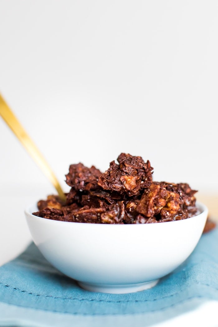 Chocolate, grain-free granola with cocoa, coconut flakes and nuts in a bowl with a gold spoon.