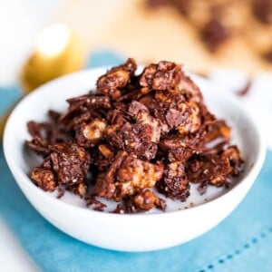 Chocolate granola in a white bowl with milk on a blue napkin.