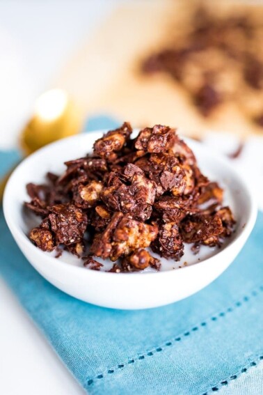 Chocolate granola in a white bowl with milk on a blue napkin.