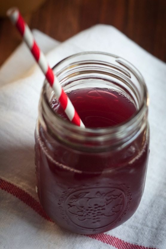 Mason jar with purple liquid and red and white striped straw sitting on a white towel. 