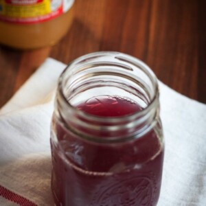 Mason jar with purple liquid and red and white striped straw sitting on a white towel.