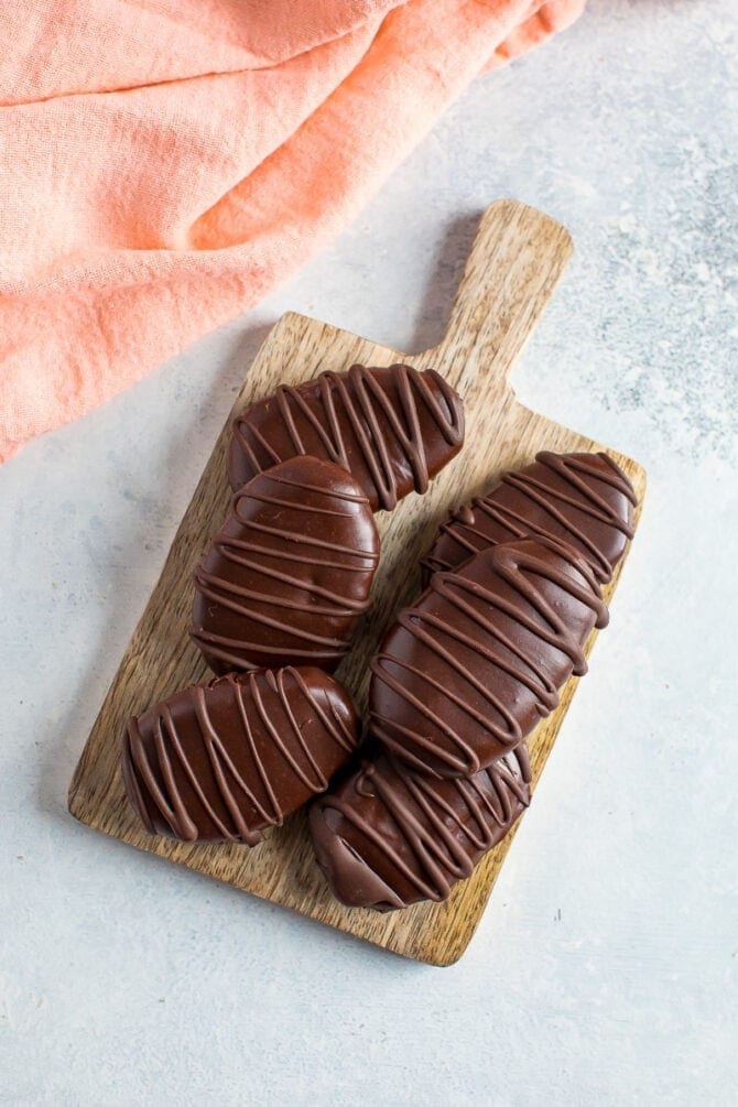 Six homemade chocolate peanut butter eggs drizzled with chocolate on a wood board. Dish cloth beside the board.