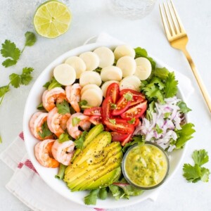 Salad in a bowl with shrimp, avocado, hearts of palm, tomatoes, and onion.