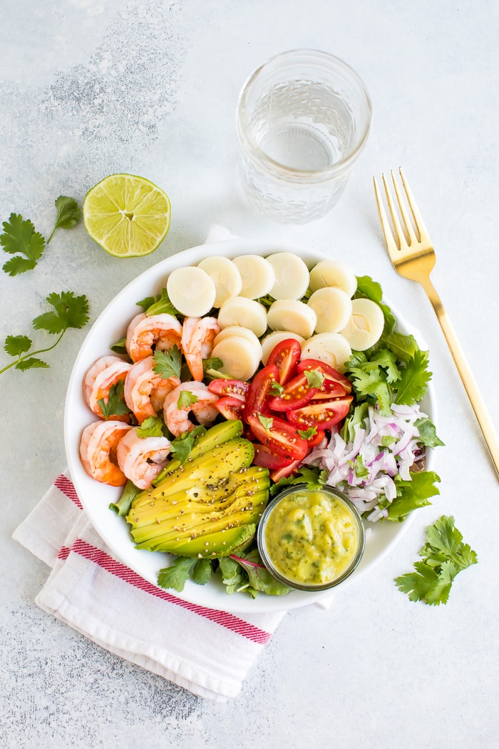 Salad in a bowl with shrimp, avocado, hearts of palm, tomatoes, and onion.