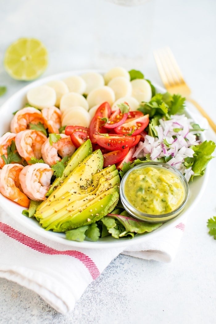 Salad in a bowl with shrimp, avocado, hearts of palm, tomatoes, and onion.