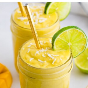 Glasses of avocado mango smoothies garnished with coconut flakes and lime slices.