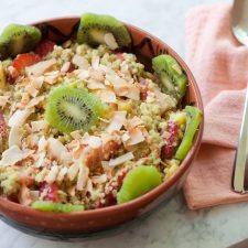 A bowl of quinoa fruit salad topped with toasted coconut and kiwi.