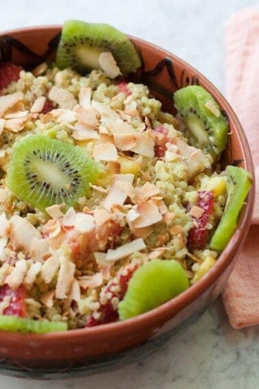 A bowl of quinoa fruit salad topped with toasted coconut and kiwi.