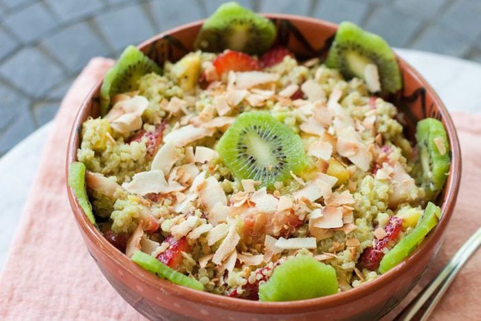 A bowl of quinoa fruit salad topped with toasted coconut and kiwi.