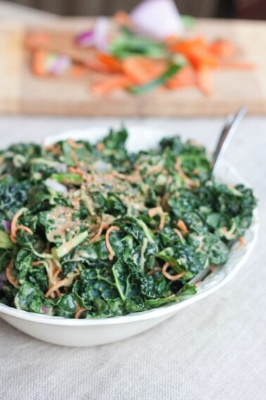 Spiralized Carrots and Cucumber Kale Salad with Peanut Sauce served in large white bowl on light grey table cloth.