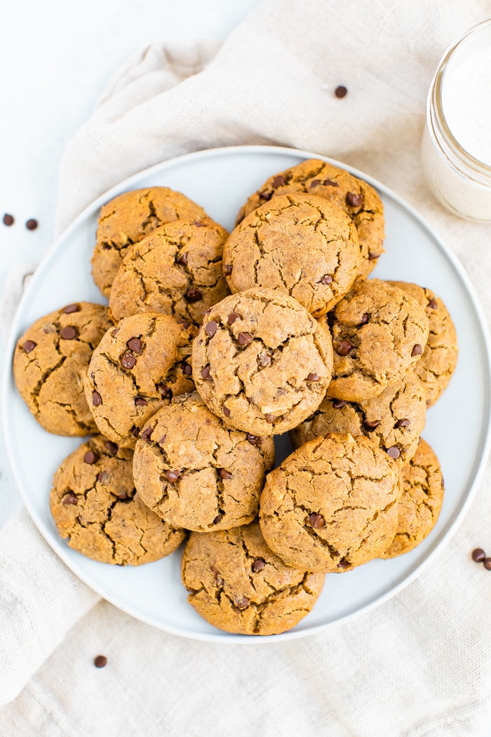 Plate with chocolate chip tahini cookies. A glass of milk is beside the plate.