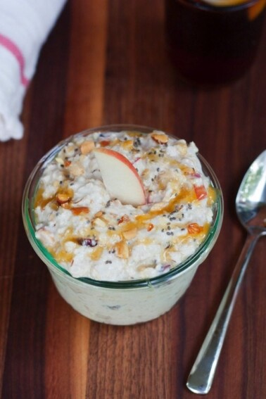 Overhead shot of Swiss Chilled Oatmeal with apples, dried fruit and nuts in a clear serving dish on wood cutting board.