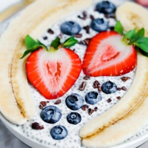 Bowl with chia pudding topped with a split banana, strawberries, blueberries and cacao nibs.