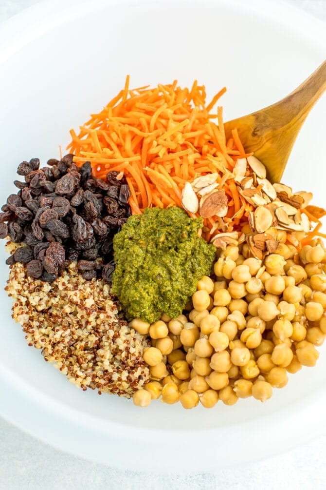 Large bowl with ingredients for a carrot raisin salad including quinoa, chickpeas, carrots, raisins and cilantro almond dressing.