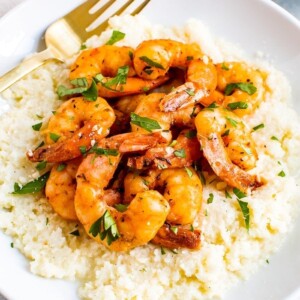 Plate of cauliflower cheese grits topped with blackened shrimp and chipped fresh parsley. A fork is resting on the plate.