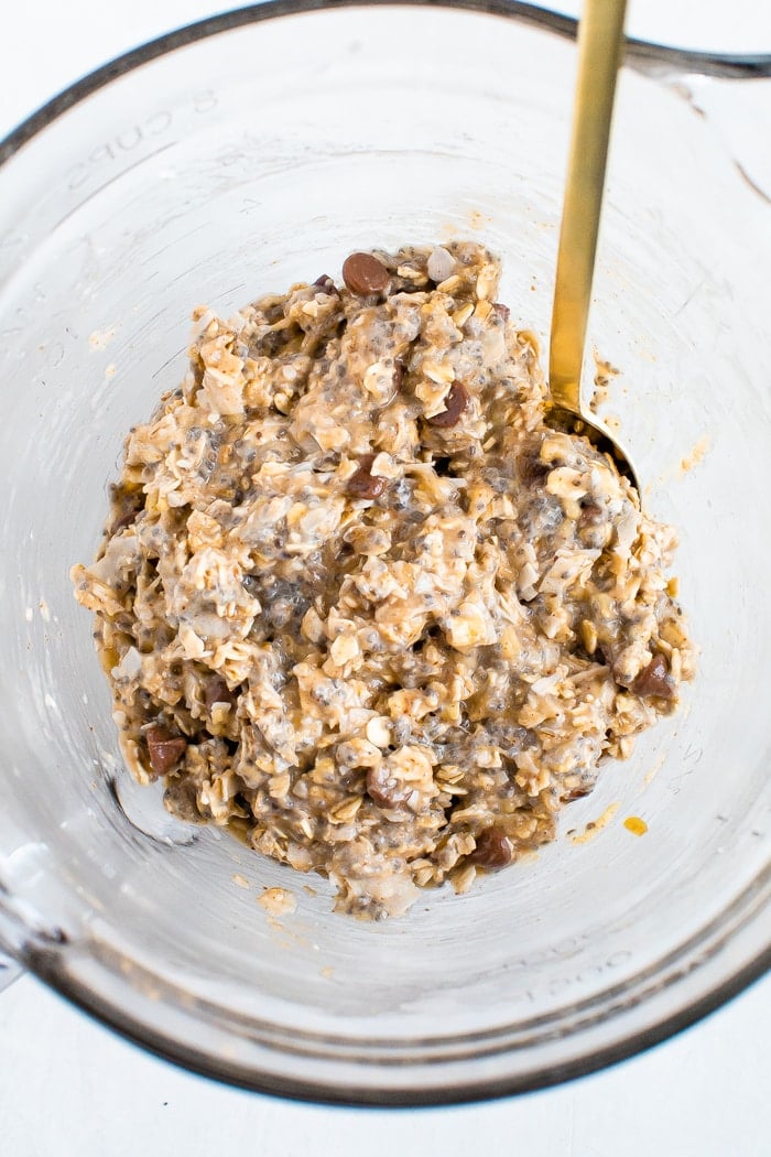 Oatmeal chia cookie batter in a glass mixing bowl with a gold spoon.