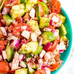 Cucumber tomato and onion salad in a blue and white bowl.