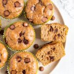 Plate of chocolate chip flourless zucchini muffins. One muffin is sliced in half and you can see the chocolate chips.