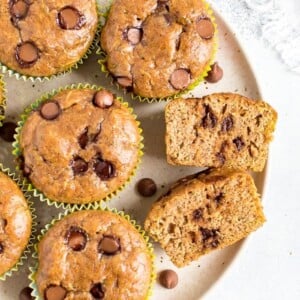 Plate of chocolate chip flourless zucchini muffins. One muffin is sliced in half and you can see the chocolate chips.