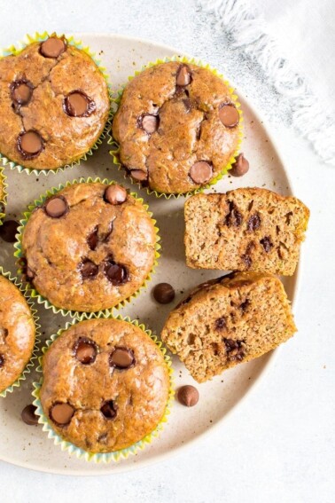 Plate of chocolate chip flourless zucchini muffins. One muffin is sliced in half and you can see the chocolate chips.