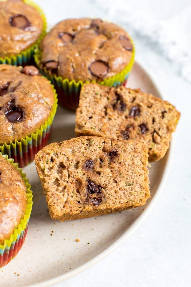 Close up plate of muffins. One muffin is sliced in half and you can see the chocolate chips.