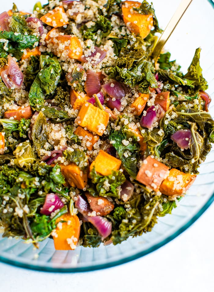 Bowl of tossed kale quinoa sweet potato salad with caramelized onions and fresh herbs.