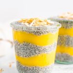 Two jars of chia pudding layered with mango puree and topped with toasted coconut flakes.