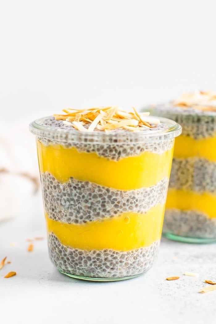 Two jars of chia pudding layered with mango puree and topped with toasted coconut flakes.
