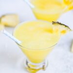 Two skinny piña coladas in glass cups with blue polka dot paper straws.