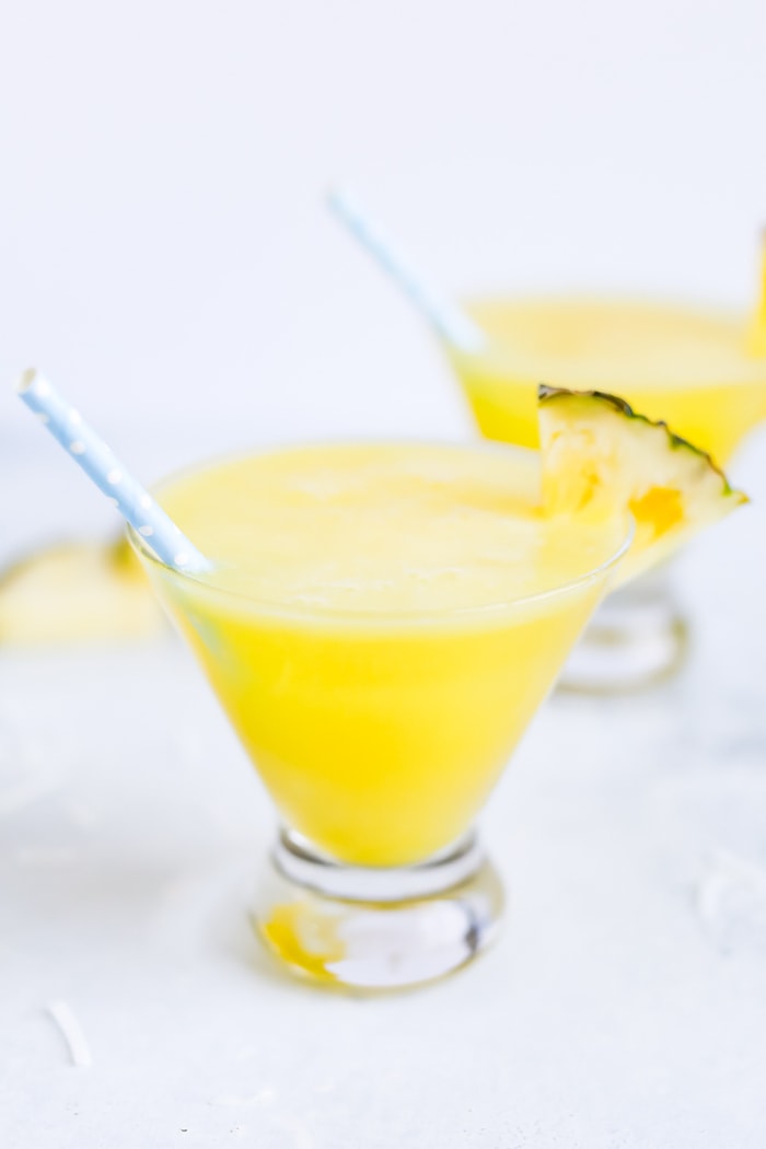 Two skinny piña coladas in glass cups with blue polka dot paper straws. 