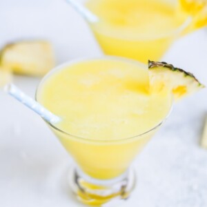 Two skinny piña coladas in glass cups with blue polka dot paper straws.