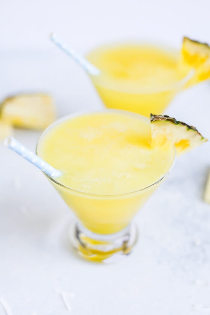Two skinny piña coladas in glass cups with blue polka dot paper straws.
