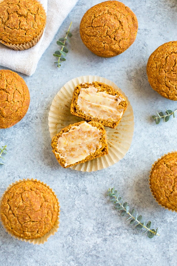 Healthy pumpkin cornbread muffins on a table with a cloth napkin and greenery sprigs. One muffin is sliced and spread with ghee.