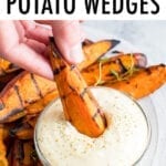 Hand dipping a grilled sweet potato wedge into a bowl of creamy dip.