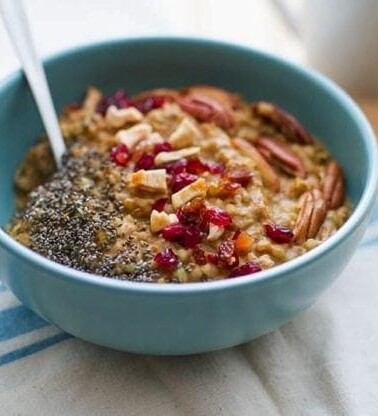 Buckwheat Pumpkin Power Bowl topped with chia seeds, dried cranberries, apples and pecans served in a light blue bowl on white dish towel.