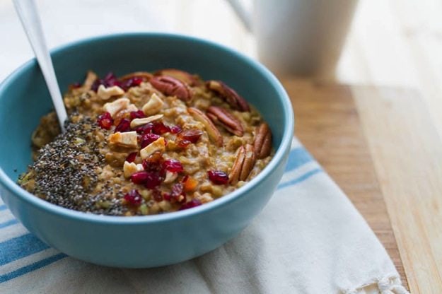 Buckwheat Pumpkin Power Bowl topped with chia seeds, dried cranberries, apples and pecans served in a light blue bowl on white dish towel.